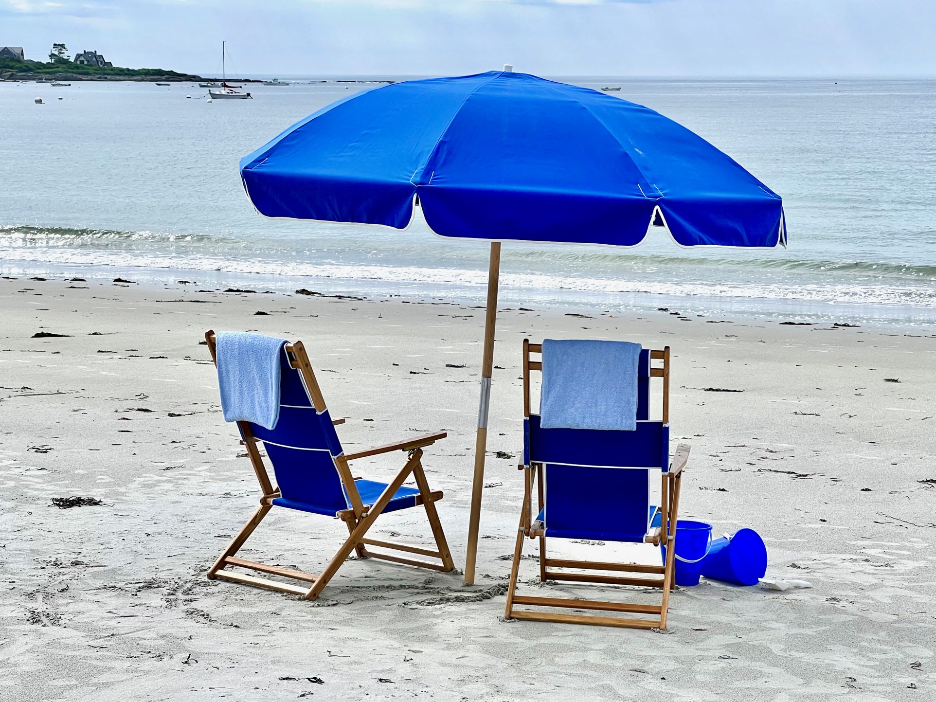 Blue Beach Chairs And Umbrella On The Beach With The Occean In The Background