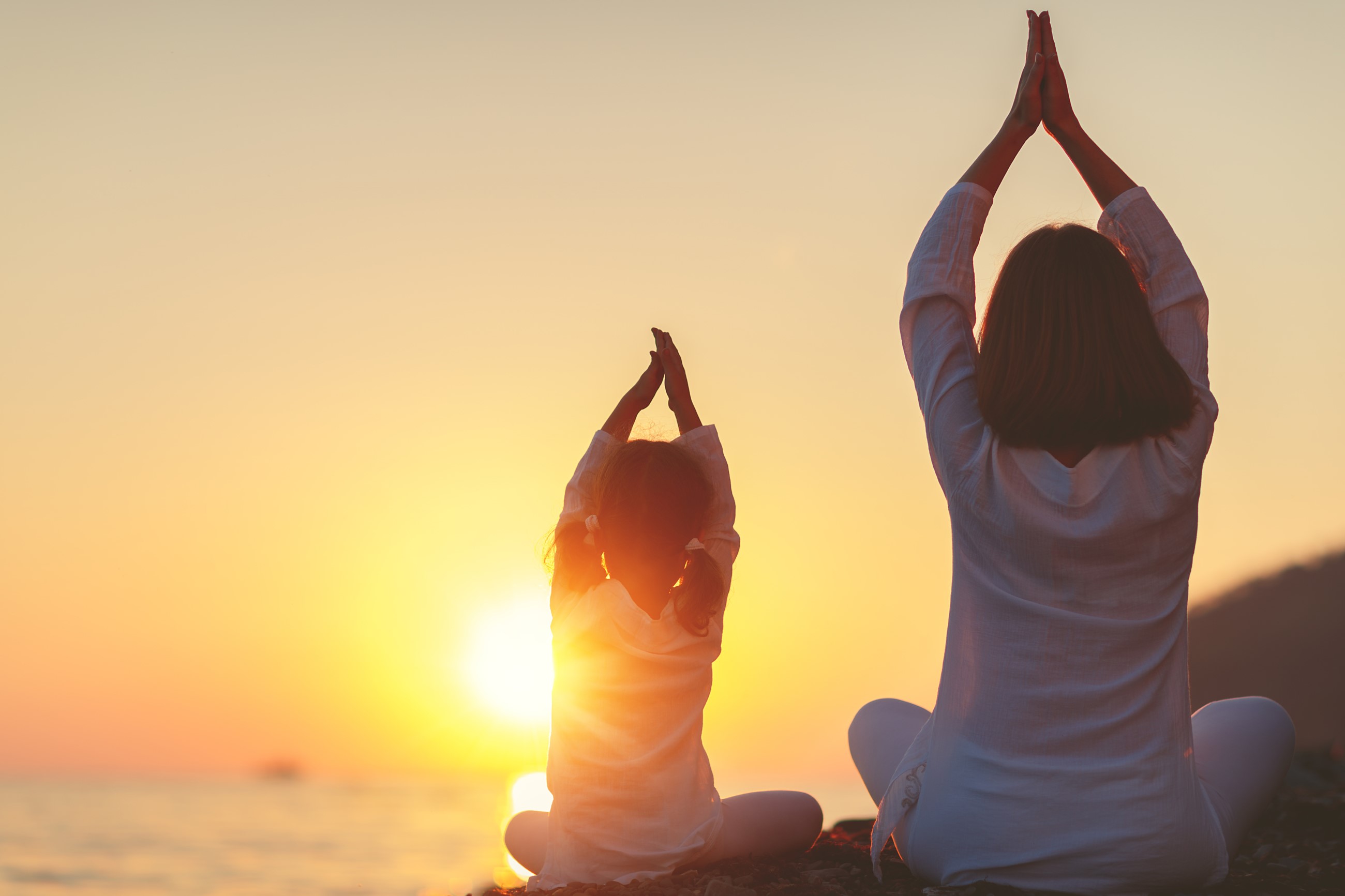 Mother and daughter doing yoga on the beach at sunrise